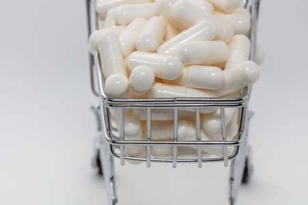 High angle shot of a small shopping cart full of white pills. White background. Close up shot. Shopping online, buying medicine, pharmaceutical business concepts.の写真素材