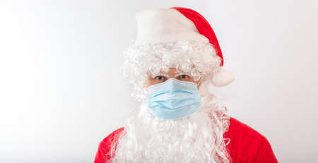 View of a man wearing a Santa Claus costume and a medical mask on white background. Man looks stressed, angry, and agitated, staring straight in the camera. New normal, new reality, holiday concepts.の写真素材