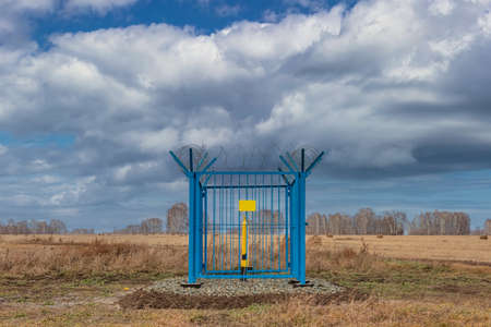 Shot of a caged industrial gas station with barbwire on top of the fence. Yellow gas pipe in the middle of the cage, empty yellow plate on the fence. Blue cloudy sky as a background. Siberia, Russia.の写真素材