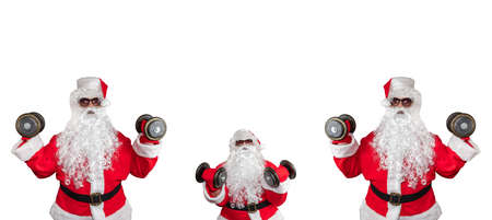 Three Santa Clauses working out, pushing and lifting dumbbells up in the air. One of them is very little and stands in the middle. Isolated on white background. Banner size, copy space.の写真素材