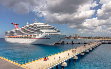 Cozumel, Mexico - March 12, 2020: Carnival Conquest docked in Cozumel. Gorgeous turquoise water and pier with tourists on it in the foreground. Cloudy blue sky in the background.のeditorial素材