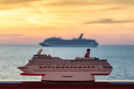 Gulf of Mexico - April 5, 2020: Small Carnival Freedom replica seating on a handrail. Blurred Carnival Valor sailing at orange sunset in the background.のeditorial素材
