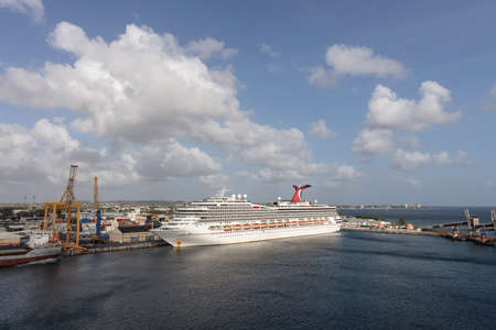 Bridgetown, Barbados - May 2, 2020: Carnival Valor docked in the port of Bridgetown. Beautiful blue sky, white clouds, port and city the background.のeditorial素材