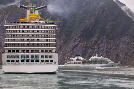 Alaska, USA - August 23, 2018: Shot of Carnival Legend sailing in one of the Alaskan Fjords. Huge mountain with some mist on top and drifting cruise ship Seabourn Sojourn in the backgorund.のeditorial素材