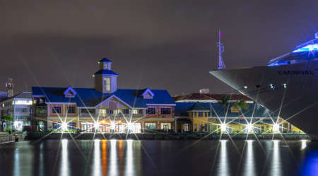 Nassau, Bahamas - July 6, 2019: Shot of the bow of Carnival Liberty cruise ship docked at Prince George Wharf at night. Light reflections in the harbor water. Port buildings in the background.のeditorial素材