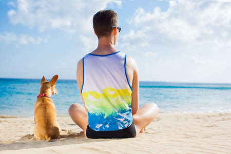 dog and owner sitting close together at the beach on summer vacation holidays, watching sunset or sunriseの写真素材