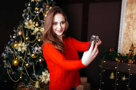 Cheerful young woman taking a Christmas selfie with smartphone. Young woman posing for a Christmas selfieの写真素材