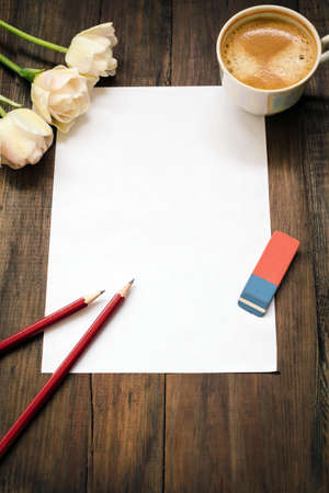 Blank sheet of white paper, red pencils, eraser, tulips and cup of coffee on dark wooden desk....