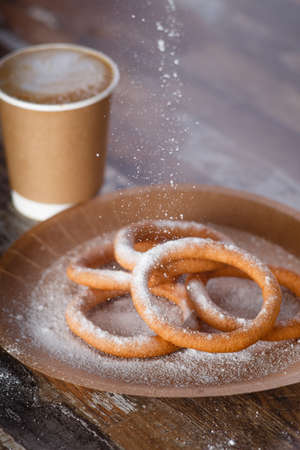 Sweet thin donuts laid out pyramid sprinkled with powdered sugar on the organic plate . Coffee in a takeaway cup. Old wood backgroundの写真素材