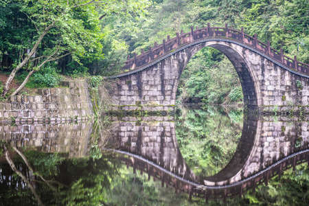 old stone bridge reflection in the waters of a quiet poolの写真素材