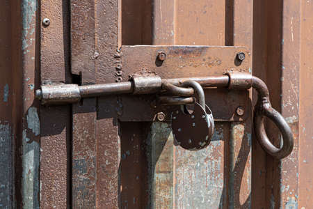 Old rusted grungy metal garage door with latch and padlock. Close up of rusty vintage lock on closed doorの写真素材