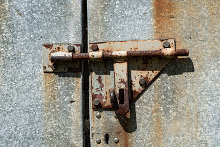 Old rusted grungy metal garage door with latch and hasp. Close up of rusty vintage lock on closed doorの写真素材