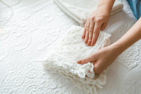 Woman folding laundry and towels in bedroom, organizing clothes in boxes and baskets. Concept of...