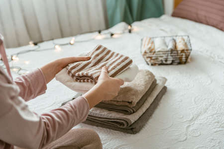 Woman folding clothes in bedroom, organizing laundry in boxes and baskets. Concept of minimalism...