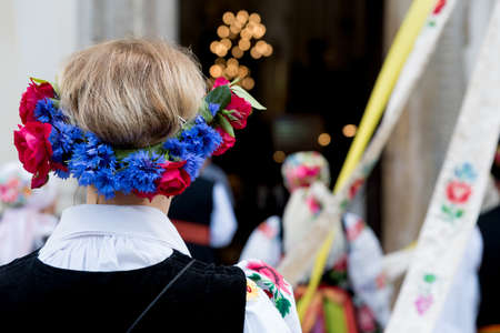 Woman with flower head wreath, dressed in polish national folk costume from Lowicz region. Traditional colorful folk dress. Rear view of floral headband, cornflower wreathの写真素材