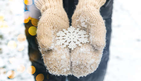 Female hands in woolen knitted winter gloves holding Christmas star decoration on snowy background. Christmas holiday and new year celebrationの写真素材