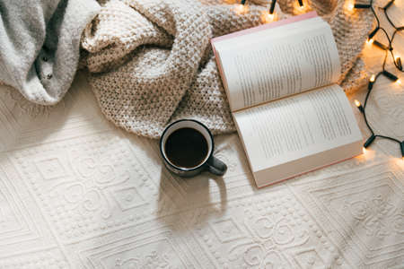 Top view of cozy blanket, open book and hot cup of coffee on bed on a cold winter day. Relaxation and hygge conceptの写真素材