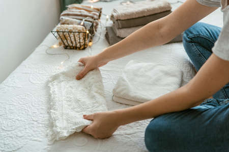 Woman folding clothes and towels in bedroom, organizing laundry in boxes and baskets. Concept of minimalism lifestyle and japanese folding system. Tidy up wardrobeの写真素材