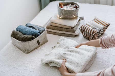 Woman folding clothes in bedroom, organizing laundry in boxes and baskets. Concept of minimalism lifestyle and japanese t shirt folding system. Tidy up wardrobeの写真素材