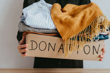 Woman holding cardboard donation box full with clothes. Concept of volunteering work, donation and clothes recycling. Helping poor peopleの写真素材