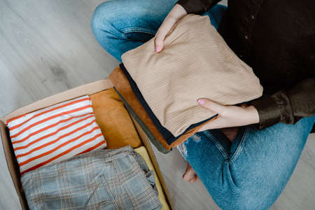 Woman folding and packing clothes into cardboard donation box. Concept of volunteering work, donation and clothes recycling. Helping poor peopleの写真素材