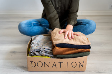 Woman folding and packing clothes into cardboard donation box. Concept of volunteering work, donation and clothes recycling. Helping poor peopleの写真素材