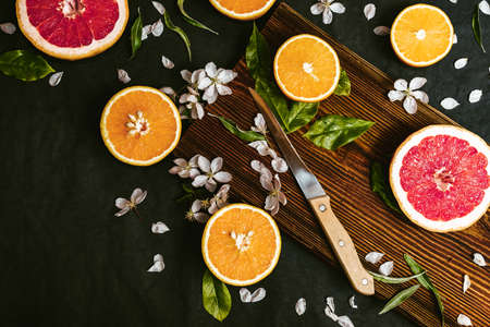 Juicy oranges and grapefruit cut in halves on wooden board on flat lay background with flowers. Preparing detox citrus juiceの写真素材