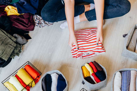 Woman folding clothes on the floor, organizing stuff in baskets and boxesの写真素材