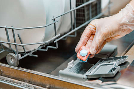 Hand putting dishwasher tablet into dishwashing machineの写真素材