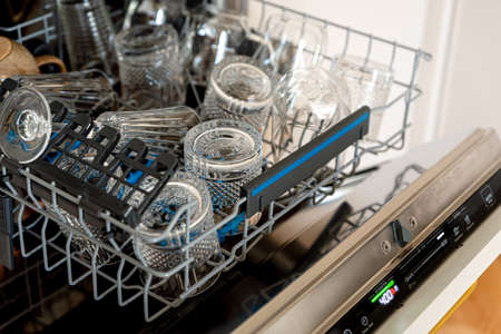 Close up of open dishwasher with crystal clear glasses and clean wine glasses on shelf. Inside...