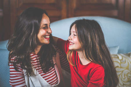 Portrait of mother and daughter are laughing and sitting together on sofa - Digital portrait of familyの写真素材