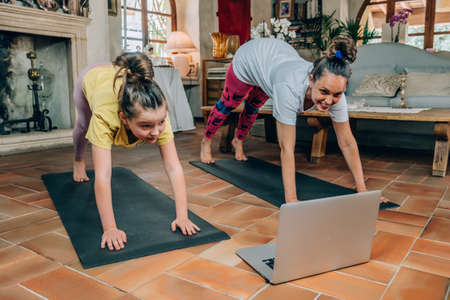 Mother and daughter practicing online yoga classes at home during the quarantine during the...