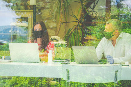 Mother and father are working with laptop at home with protective mask - Man and woman are working in office with protective mask and security distance - Self-isolation for pandemic covid19の写真素材