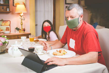 Father with his dauther are starting to have breakfast in hotel with a protective mask and social...