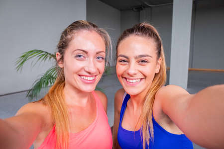 Two sporty girl taking a selfie photo with mobile phone at gym - Two beautiful female friends taking a selfie photo after hard workout in gymの写真素材