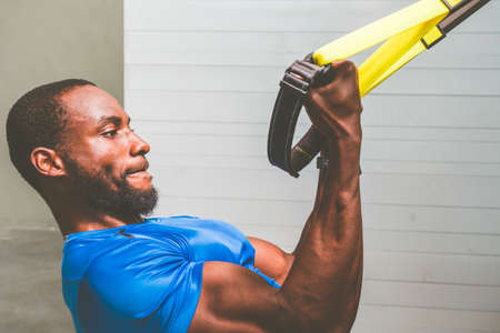 Young black personal trainer training arms with fitness straps in gym