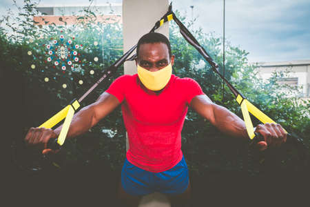 Afro american man training her arms with protective mask and straps Fitness in the gym during quarantine time for pandemic covid19の写真素材