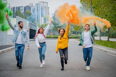 Beautiful young guys stand street and hold light up colored smoke bombs - Happy friends having fun...