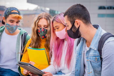 Multiethnic students sitting with mask on the bench together in a university - Group of young teenagers studying on the bench with protective mask in pandemic covid 19 periodの写真素材