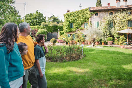 Back view of happy family hugging is standing outside their new house - This photo canuse for family, father, mother and home conceptの写真素材