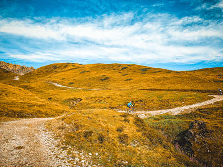 Man going with mountain bike in a mountain route - Young mountain biker riding his e-bike on a trail going through meadows - Mountain biking is a fun and challenging sportの写真素材