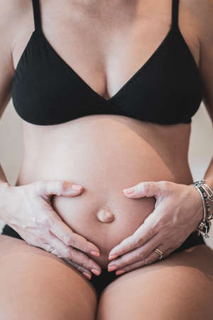 Close up picture of pregnant woman and her baby holding her belly - Baby holding the belly of his pregnant mother - Pregnant woman and her baby holding hands together - Love for family, parenting picture of pregnant woman hugging her belly with her hands - Close-up of hands forming a heart on the belly of a pregnant woman - Love for family, parentingの写真素材