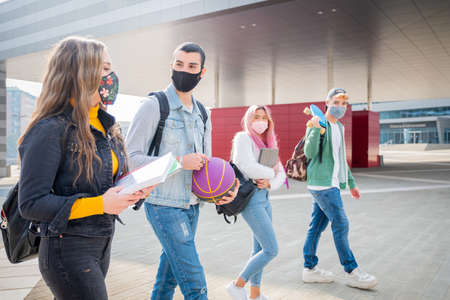 Multiracial students with face mask walking speaking wearing protective mask during pandemic codvid19 at college campus - New normal lifestyle with social distance in coronavirus timeの写真素材