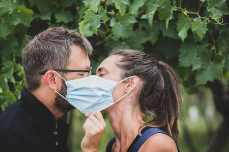 Couple of lovers kissing behind protective mask - New normal lifestyle concept with couple in love kiss outdoorの写真素材