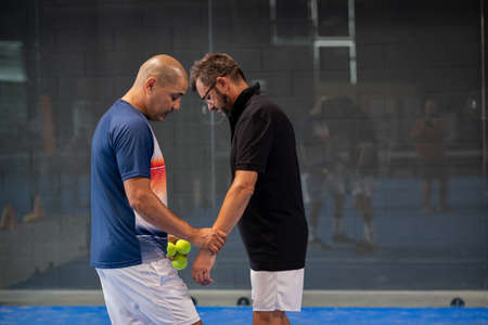 Monitor teaching padel class to man, his student - Trainer teaches boy how to play padel on indoor tennis courtの写真素材