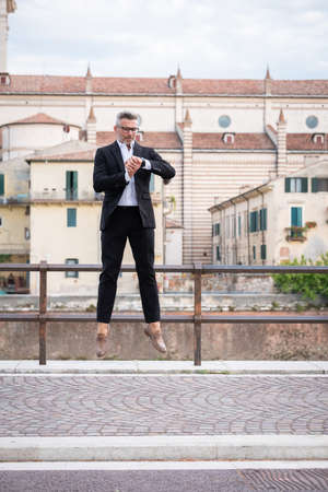 Handsome businessman checking the time on his watch and jumping from stationary. Strange and surreal situationの写真素材