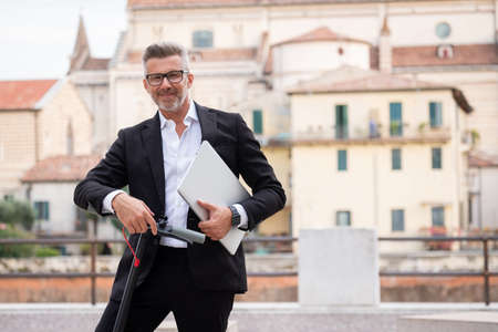 Handsome man works online freelancer or businessman pulls out laptop with backpack and electric scooter. Active lifestyle, backpacker traveler. Ecology and clean ecological mode of transportの写真素材