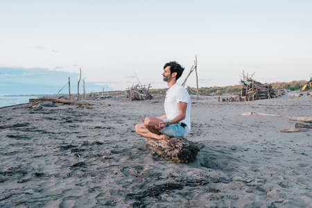 Caucasian boy practicing yoga by the sea at sunrise - Man practicing yoga pose to meditation on the beach at sunset - Healthy with yoga conceptの写真素材