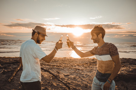 Cheerful young people spending time together on the beach and drinking beer and toasting at the beach on vacation in twilight summer sunset. Friendship conceptの写真素材