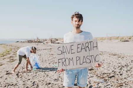 Group of activist friends collecting plastic waste on the beach. People cleaning the beach, with bags. Concept of environmental conservation and ocean pollution problemsの写真素材